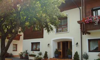 An inviting house with a large tree and blooming plants. The entrance area is friendly and brightly designed.