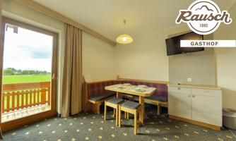 A cozy guesthouse room with a table and chairs. The windows offer a view of the greenery, and the room is bright and inviting.