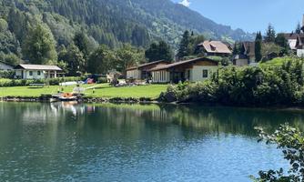 A picturesque landscape with a clear lake and green meadows. In the background, there are mountains and pretty cottages.