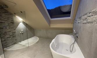 A modern bathroom in the attic with a shower cabin and a freestanding bathtub. Large windows provide plenty of daylight and a pleasant atmosphere.