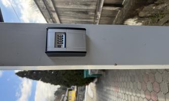 An electronic locker is mounted on a post. In the background, a paved path and a wooden wall are visible.