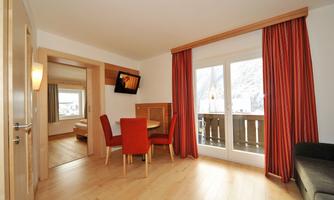 A modern living room with a round table and red chairs. There are large windows with a view outside and cozy furniture.
