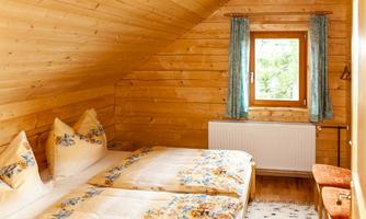 A cozy bedroom with wooden walls and a sloped ceiling. There are two beds with floral bedspreads and a window with a view.