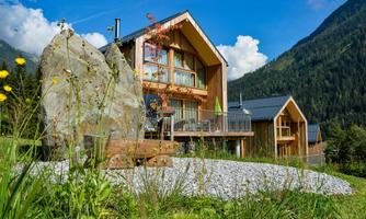 Modern wooden houses in a picturesque mountain landscape.  
Surrounded by lush greenery and under a clear blue sky.