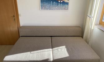 A cozy, gray sofa is in a bright room. A colorful picture of a harbor hangs on the wall.