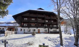 A charming chalet in the snow with multiple balconies. Surrounded by a winter landscape and trees.
