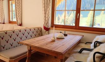 A cozy dining area with a wooden table and a sofa. Large windows offer a view of the surrounding nature.