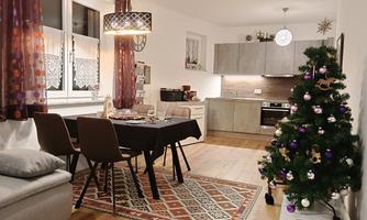 A cozy living room with a dining table, chairs, and a Christmas tree. The warm colors and the decorations create an inviting atmosphere.