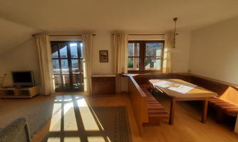 A bright and cozy living room with large windows. The dining area is furnished with a table and benches.