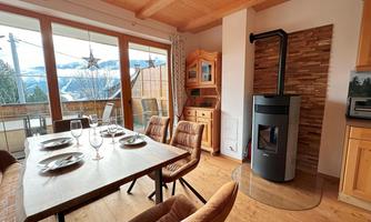 A cozy dining area with a wood stove and large windows that offer a view of the mountains. The table is beautifully set and the decor is modern and inviting.