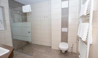 A modern bathroom with a glass shower and light tiles. Towels are hanging on a radiator.