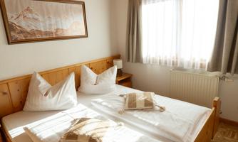 A cozy bedroom with a double bed and two decorative pillows. Bright colors and natural light create an inviting atmosphere.