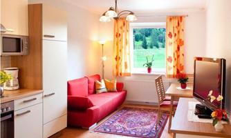 A cozy living room with a red couch and a small table. Large windows provide plenty of light and a view of the green landscape.