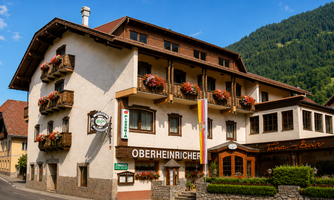 A charming house with balconies full of flowers and an inviting facade. The surroundings showcase picturesque mountains and a quiet street.