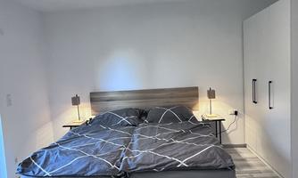 A modern bedroom with a double bed and gray ceilings. There are two nightstands and a large wardrobe against the wall.
