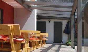 A large, covered outdoor area with wooden tables and benches. The floor is paved with colorful stones and there is plenty of daylight.