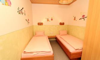 A bright children's room with two beds and colorful owl pictures on the wall. The room has a friendly atmosphere and is simply furnished.