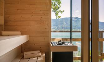An elegant sauna with wooden paneled walls and a large window front. Outside is a beautiful view of the lake and the surrounding mountains.