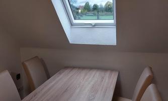 A bright room with a wooden table and beige chairs. The window offers a view of the landscape outside.