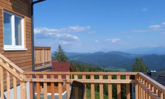 A balcony with a view of the mountains and the blue sky. The wooden structure of the balcony creates an inviting atmosphere.