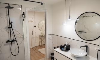A modern bathroom with a walk-in shower and elegant fixtures. The large round mirror and the simple color scheme create a stylish ambiance.