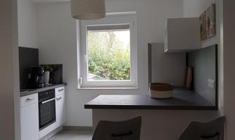 A modern kitchen with a small dining area. There is a view of the garden through the window.