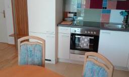 A modern kitchen with a wooden table and two chairs. The kitchen unit has colorful tiles and is well equipped.
