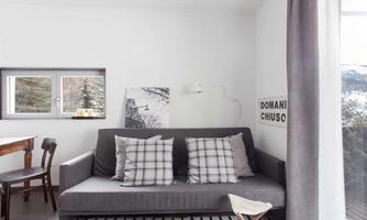 A modern living room with a gray sofa and checkered cushions. Large windows let in plenty of light and offer a view of nature.