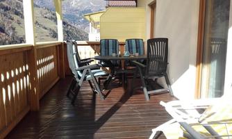 A cozy balcony with a table and chairs. The sun terrace offers a view of the surrounding mountain landscape.