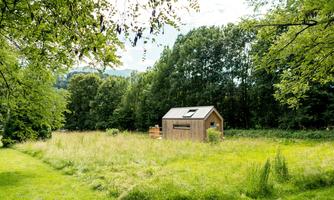 A small wooden house stands amidst a green meadow. Surrounded by trees and untouched nature, the scene radiates tranquility and idyll.