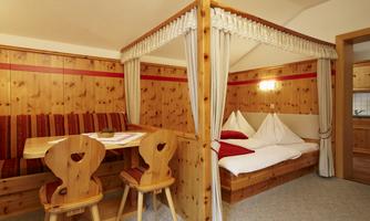 A cozy room with wood paneling and a canopy bed. A dining table with chairs is also available.