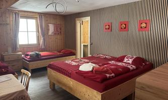 A cozy bedroom with two beds and a warm wood decor. On the walls are red pictures and curtains, and the light shines through a window.