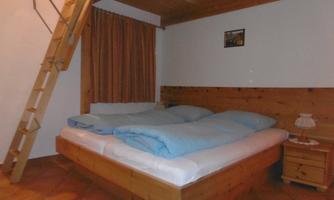 A cozy bedroom with a large double bed and blue bed sheets. A wooden staircase leads to a sleeping area above.