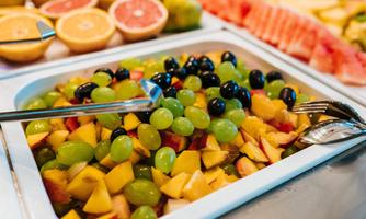 A colorful fruit salad with grapes, apples, and other fruits. In the background, you can see more fresh fruits.