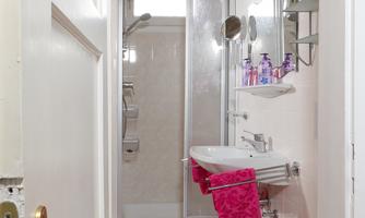 A small, modern bathroom with a shower and sink. Pink carpets and towels give the room a fresh touch.