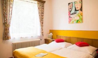 A cozy bedroom with two beds and yellow pillows. A colorful painting hangs on the wall.