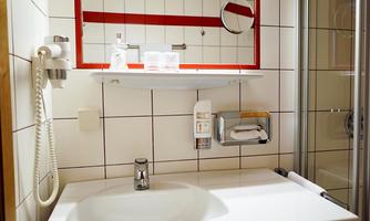 A modern bathroom with a sink and mirror. The walls are tiled and there is a shower area.