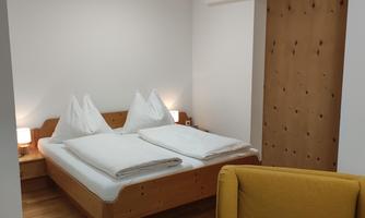 A cozy bedroom with a double bed and two bedside tables. A comfortable, yellow armchair is also in the room.