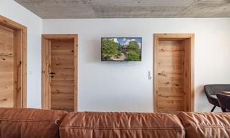 A modern living room with a brown leather couch and a TV on the wall. There are two wooden doors on the sides.