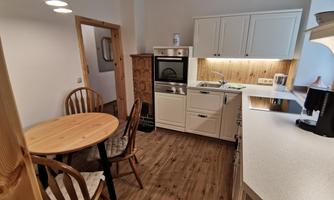 A modern kitchen with a round wooden table and chairs. The white cabinets and the wooden paneling create an inviting atmosphere.