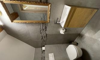 A modern bathroom with a toilet and a small wash station. The room has elegant gray walls and a golden mirror.