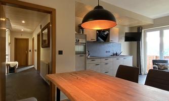 A modern kitchen with a large wooden table and a cozy atmosphere. The room is well-lit and has access to a balcony.