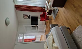 A cozy room with a double bed, a red armchair, and a wall-mounted TV. Large windows let in plenty of light and create a pleasant atmosphere.