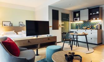 A modern apartment with a cozy living area, a television, and a kitchenette. The decor is bright and inviting with stylish furniture.