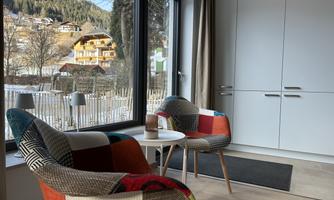 A cozy room with colorful chairs and a round table. Large windows offer a view of the mountains and nature outside.
