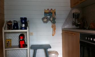 A cozy kitchen corner with a shelf full of equipment and a blue table. On the wall, pot holders and a collection of cooking utensils are hanging.