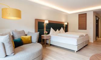 A modern hotel room with a large bed and a cozy seating area. The decor is bright and inviting, with warm lighting accents.