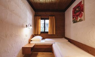 A simple bedroom with two single beds and wooden details.  

Bright curtains and a small window create a friendly atmosphere.