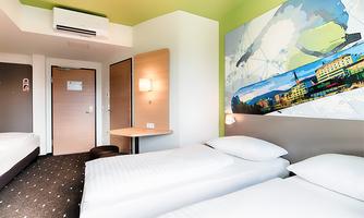 A modern room with two single beds, a table, and a colorful mural. The walls are bright, and the room is well-lit.