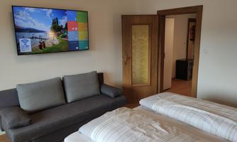 A cozy room with a sofa and two beds. A large television hangs on the wall showing a picture of a landscape.